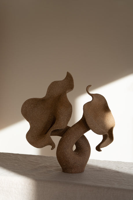 A striking piece of ceramic art, featuring a soft, seductive shell contrasted with raw, coarse textures. The vessel, crafted from textured matte grog stoneware with a brown exterior and glazed interior, evokes a dramatic allure and delicate inner essence. 