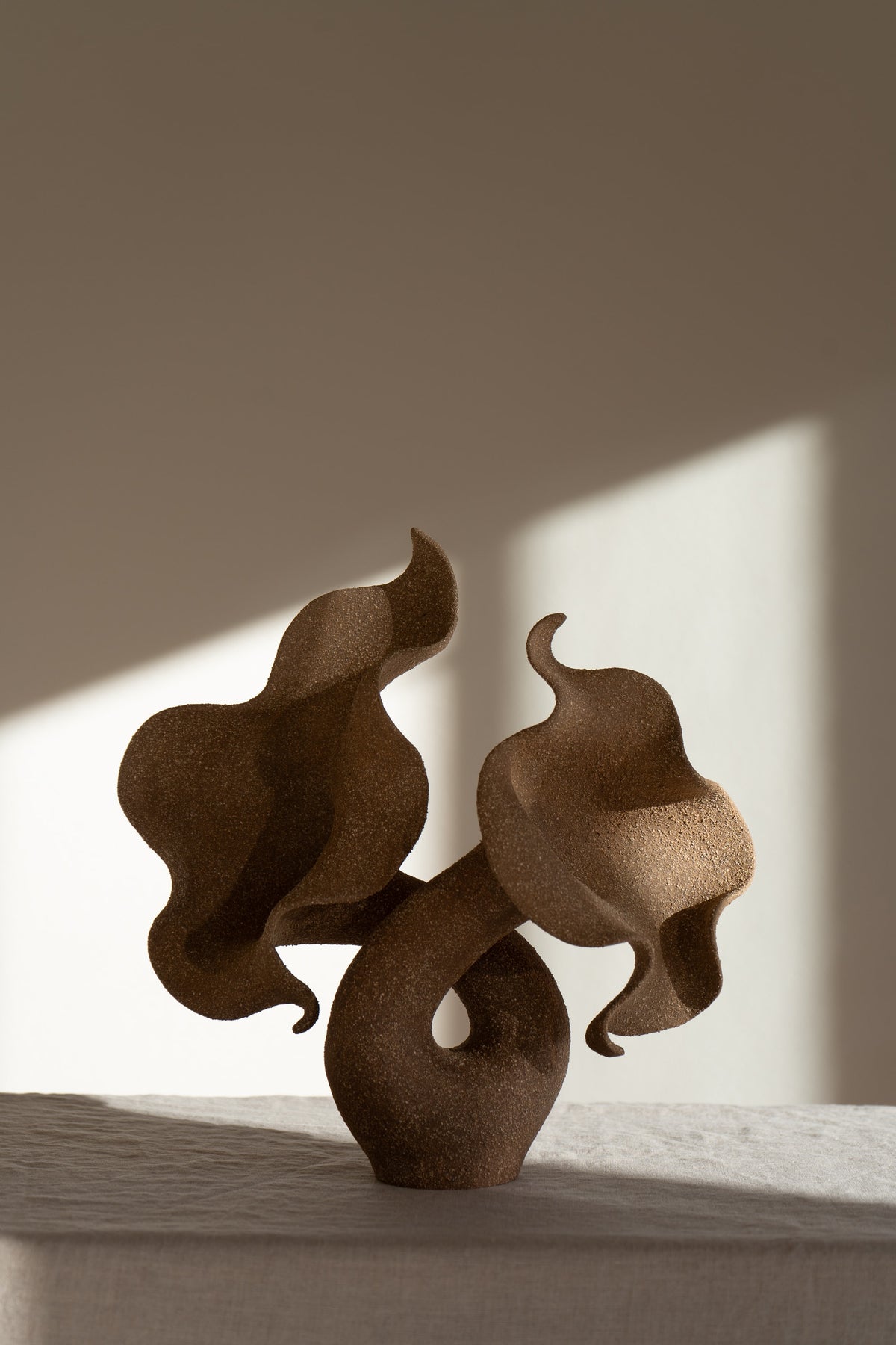 A striking piece of ceramic art, featuring a soft, seductive shell contrasted with raw, coarse textures. The vessel, crafted from textured matte grog stoneware with a brown exterior and glazed interior, evokes a dramatic allure and delicate inner essence. 