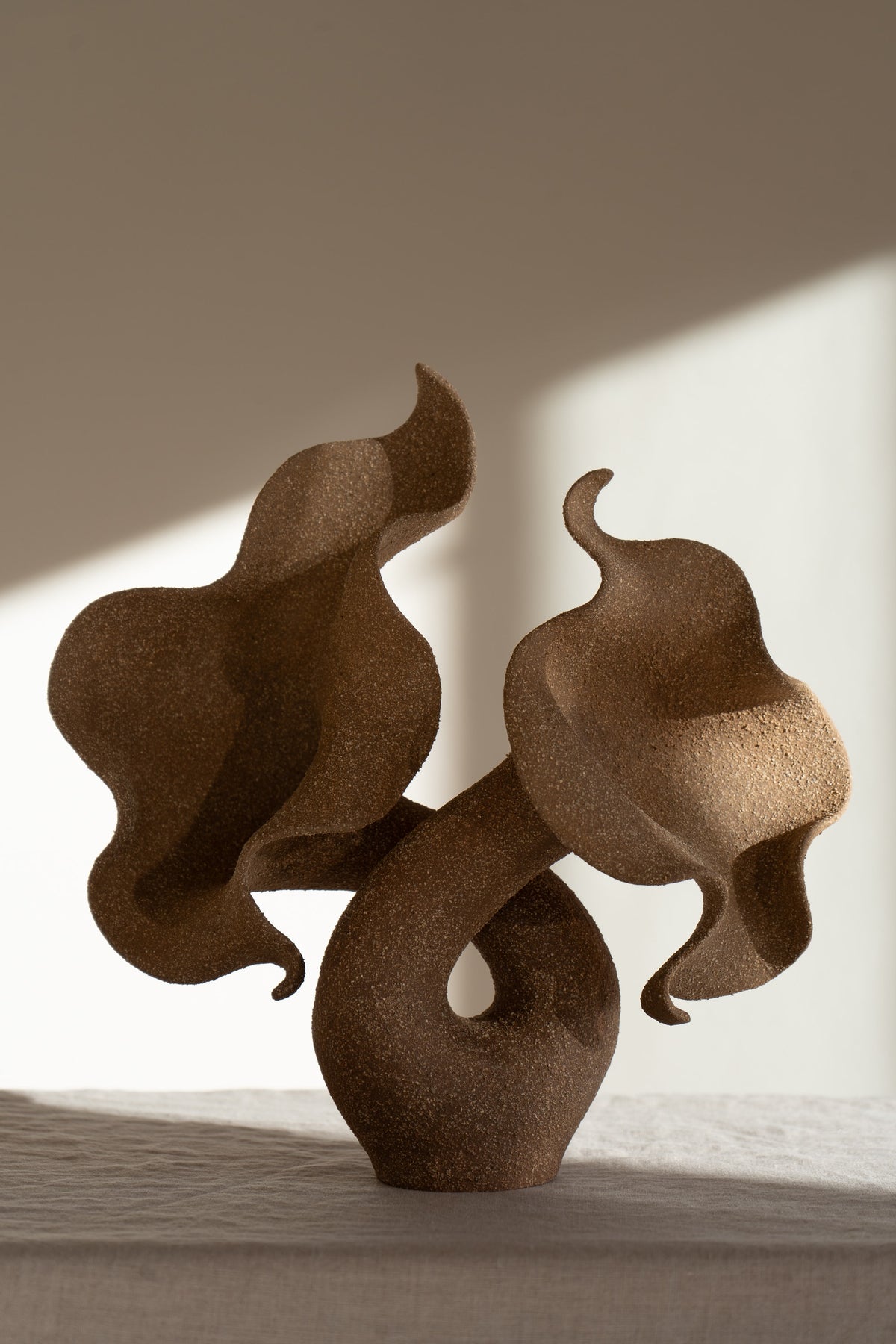 A striking piece of ceramic art, featuring a soft, seductive shell contrasted with raw, coarse textures. The vessel, crafted from textured matte grog stoneware with a brown exterior and glazed interior, evokes a dramatic allure and delicate inner essence. 