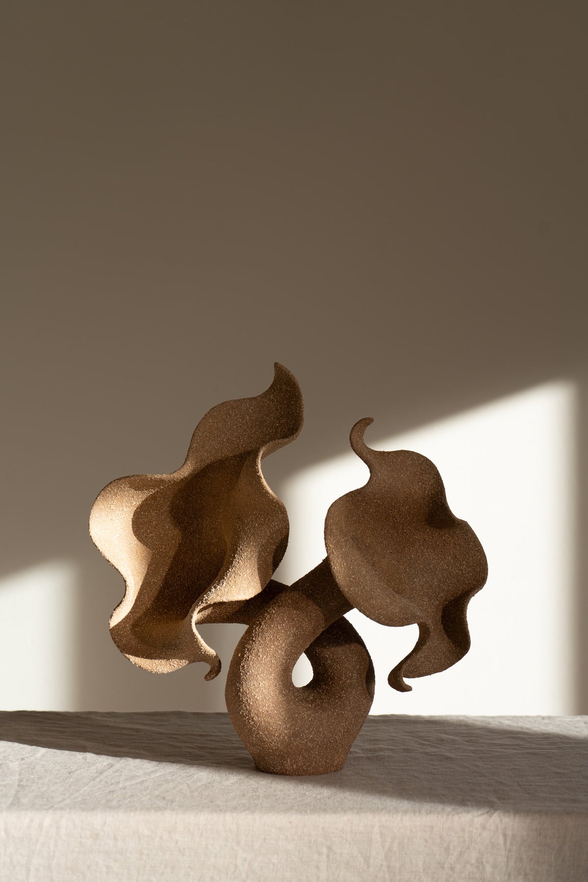A striking piece of ceramic art, featuring a soft, seductive shell contrasted with raw, coarse textures. The vessel, crafted from textured matte grog stoneware with a brown exterior and glazed interior, evokes a dramatic allure and delicate inner essence. 