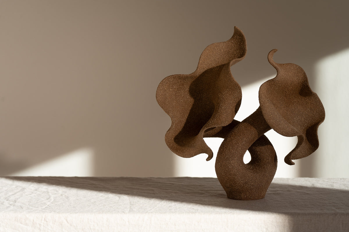 A striking piece of ceramic art, featuring a soft, seductive shell contrasted with raw, coarse textures. The vessel, crafted from textured matte grog stoneware with a brown exterior and glazed interior, evokes a dramatic allure and delicate inner essence. 
