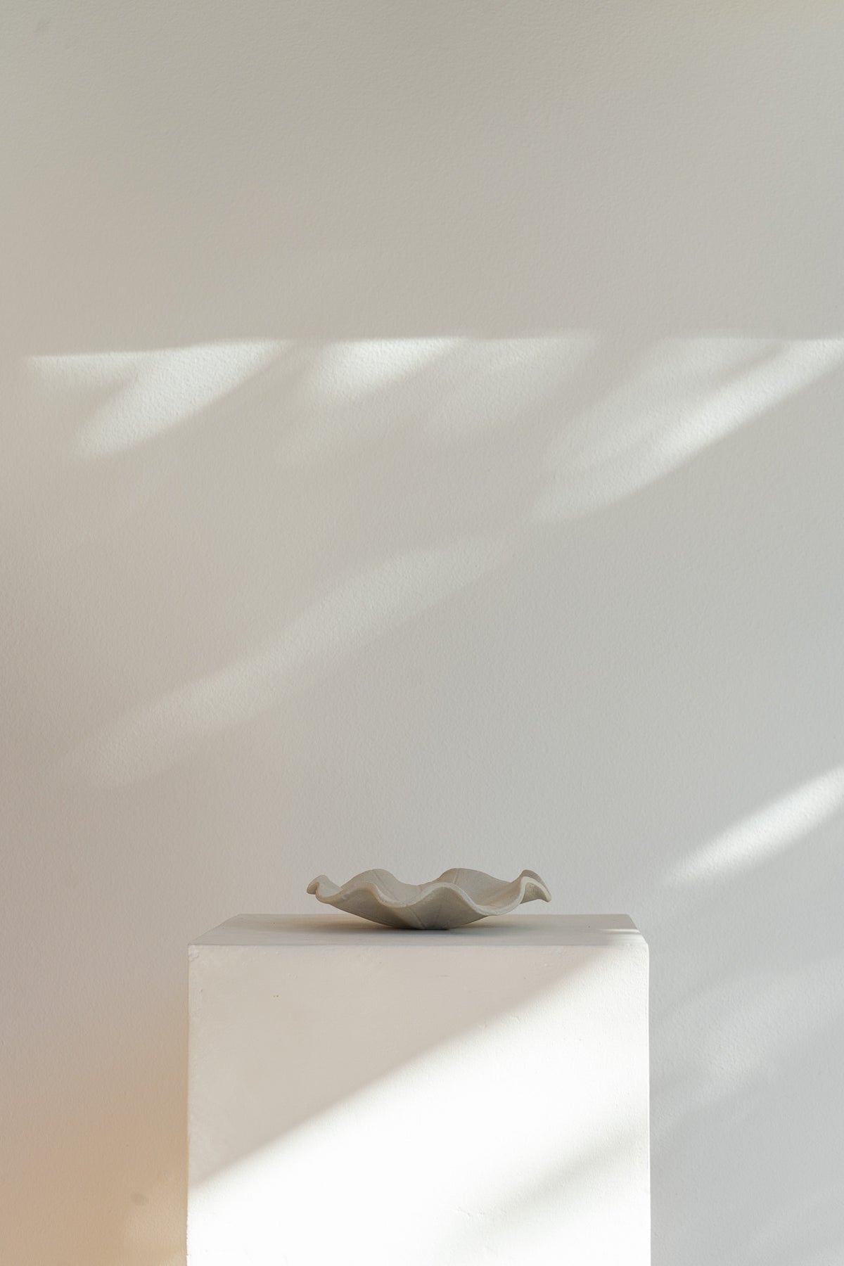 A low handmade ceramic tray with a wavy edge. The tray has a light brown, slightly textured surface 