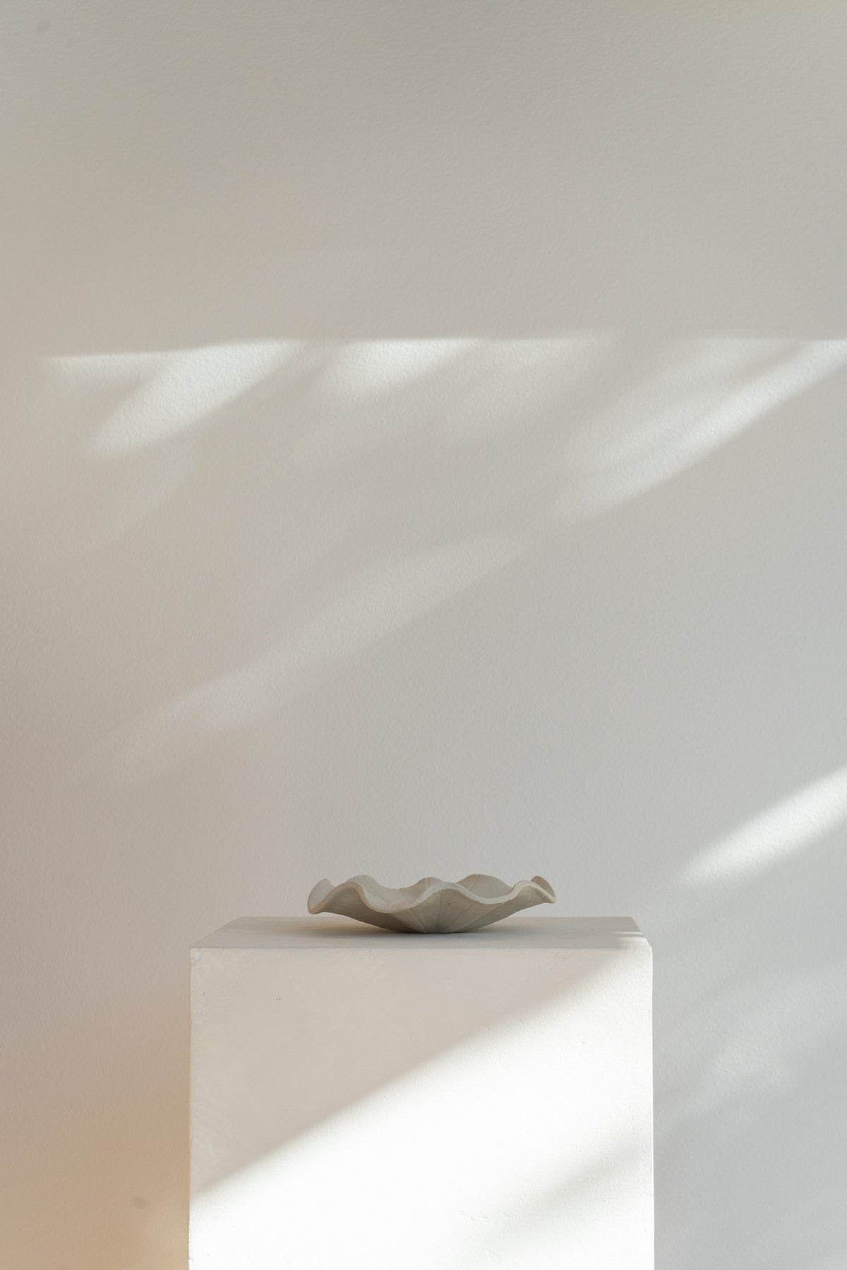 A low handmade ceramic tray with a wavy edge. The tray has a light brown, slightly textured surface 