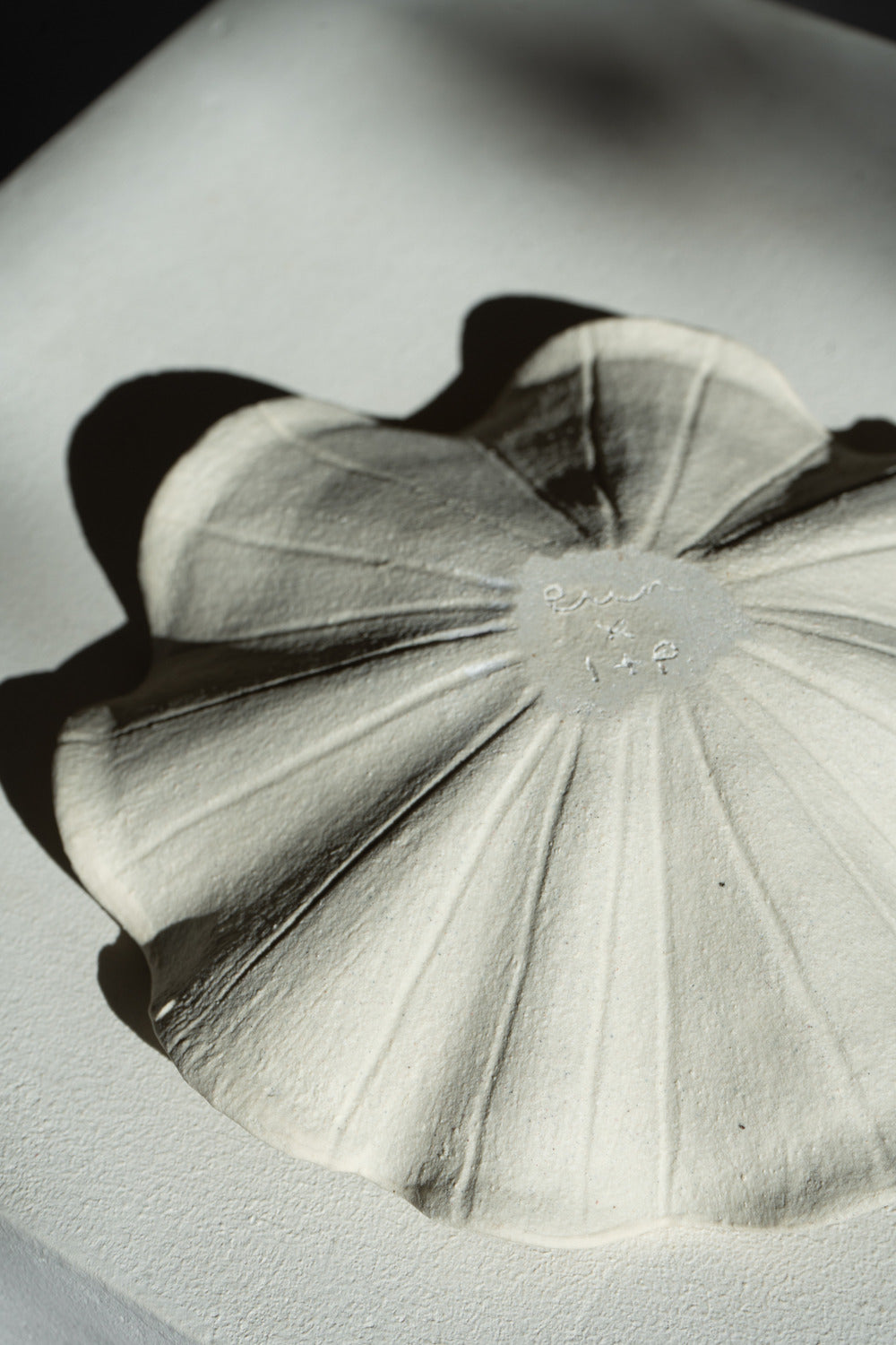 A low handmade ceramic tray with a wavy edge. The tray has a light brown, slightly textured surface 