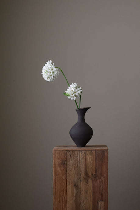 Rei Vase in Black Clay with its gently curved form and matte black finish embodies quiet sophistication. The textured glaze and subtle silhouette reflect the hand of the maker, offering a grounded, contemplative presence