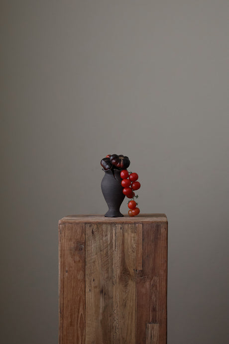 Blossom Bud Vase in Black Clay is a hand-built black clay vase features soft curves, a ruffled rim, and a speckled, tactile surface. Each form is one of a kind, shaped by hand to reflect the raw elegance of nature.