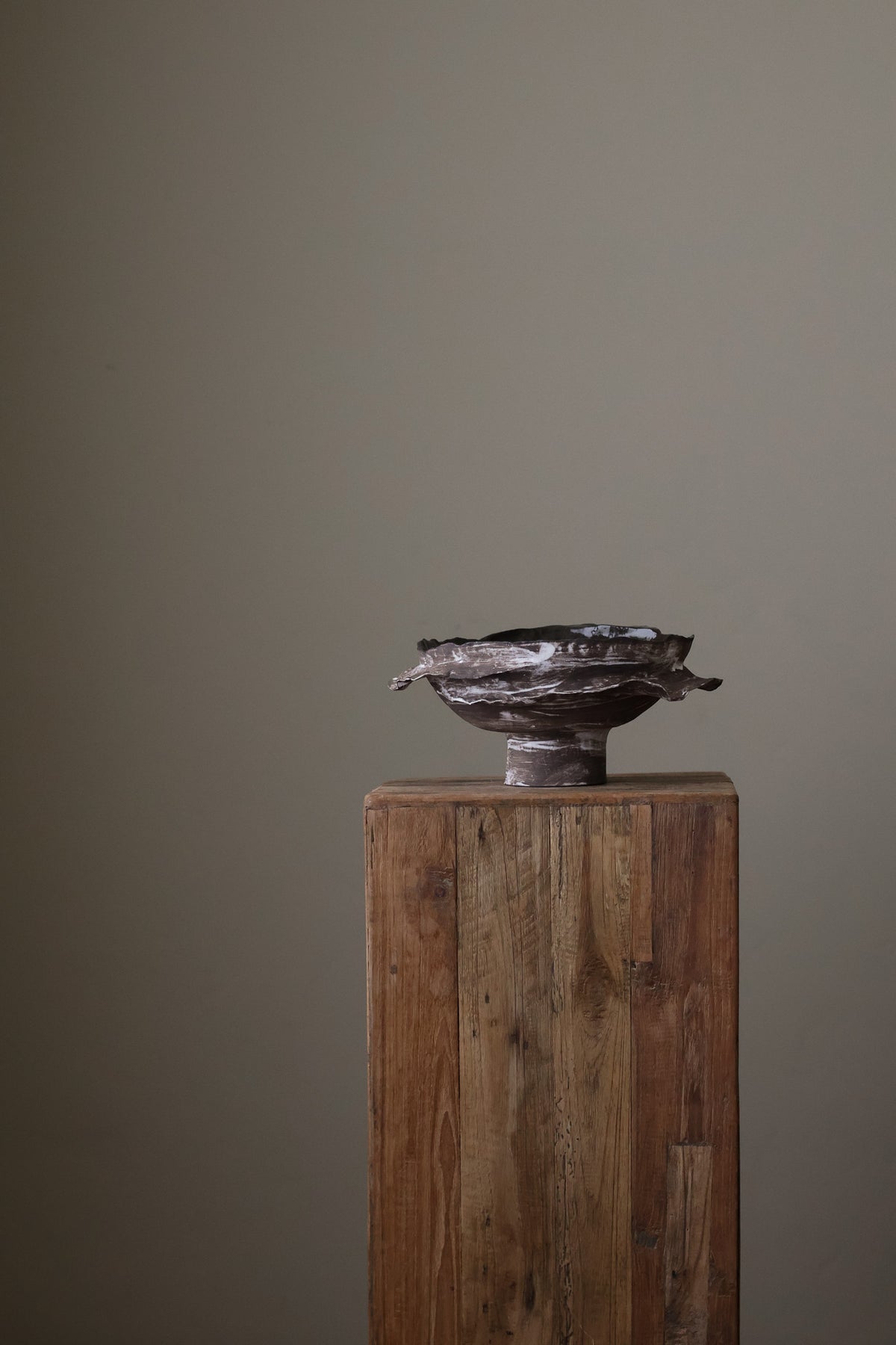 Layered Brown Pedestal Bowl is a Handcrafted ceramic piece with raw, textured dark clay finish and organic wavy rim, featuring sculptural asymmetry