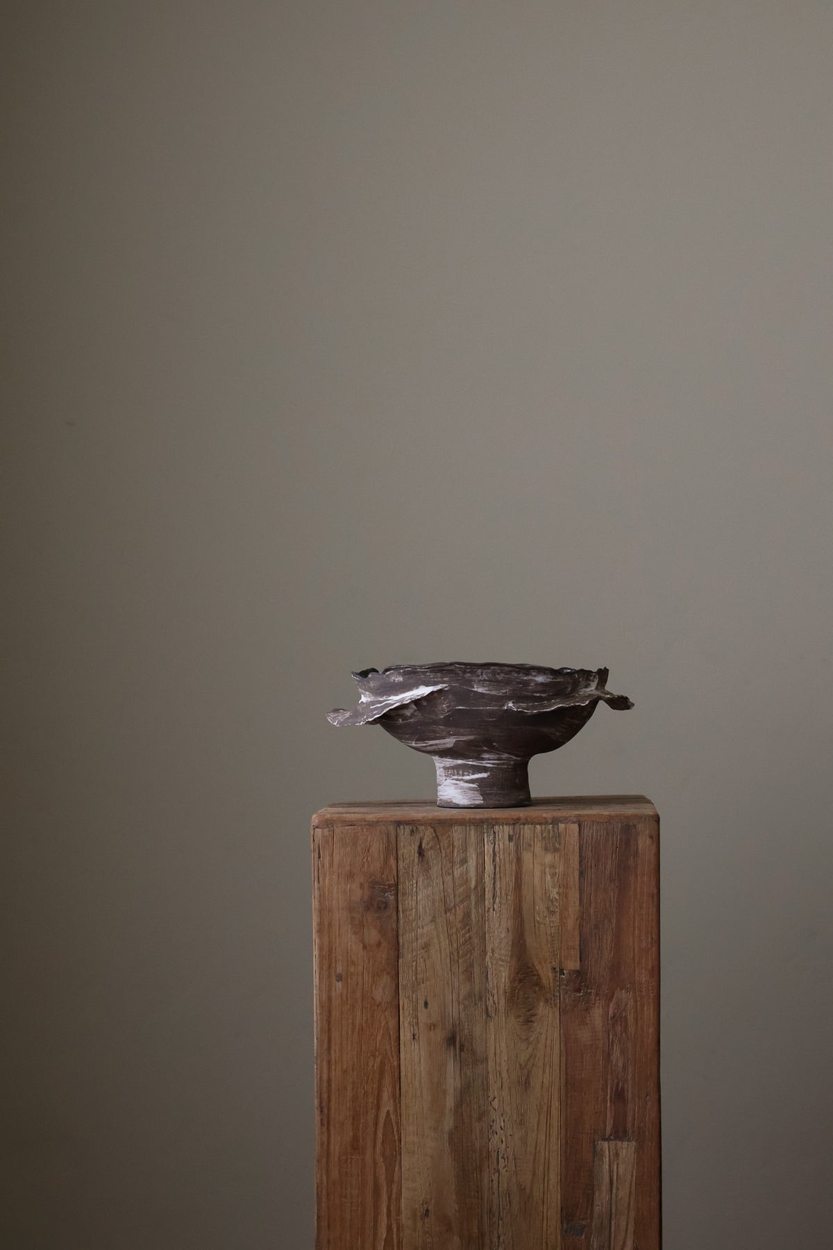 Layered Brown Pedestal Bowl is a Handcrafted ceramic piece with raw, textured dark clay finish and organic wavy rim, featuring sculptural asymmetry
