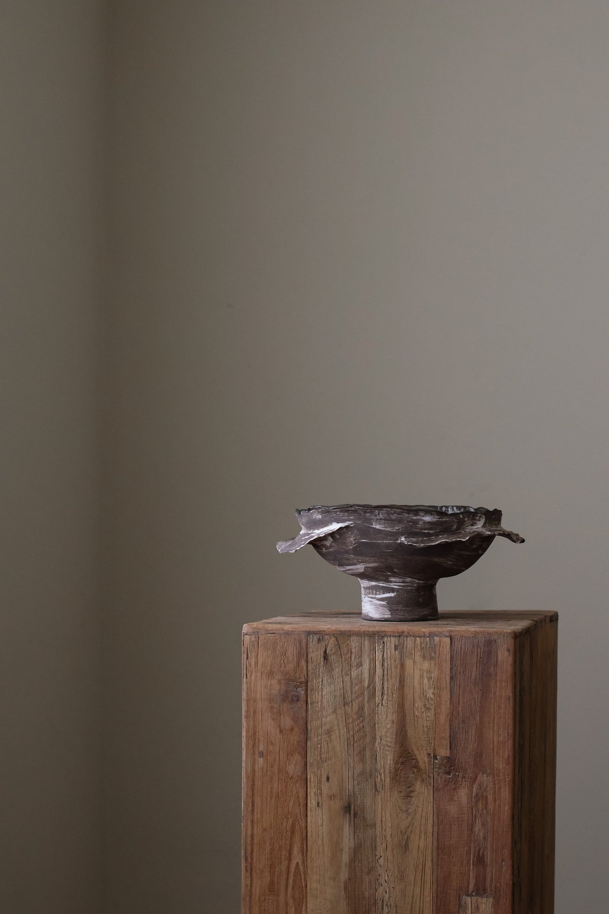 Layered Brown Pedestal Bowl is a Handcrafted ceramic piece with raw, textured dark clay finish and organic wavy rim, featuring sculptural asymmetry