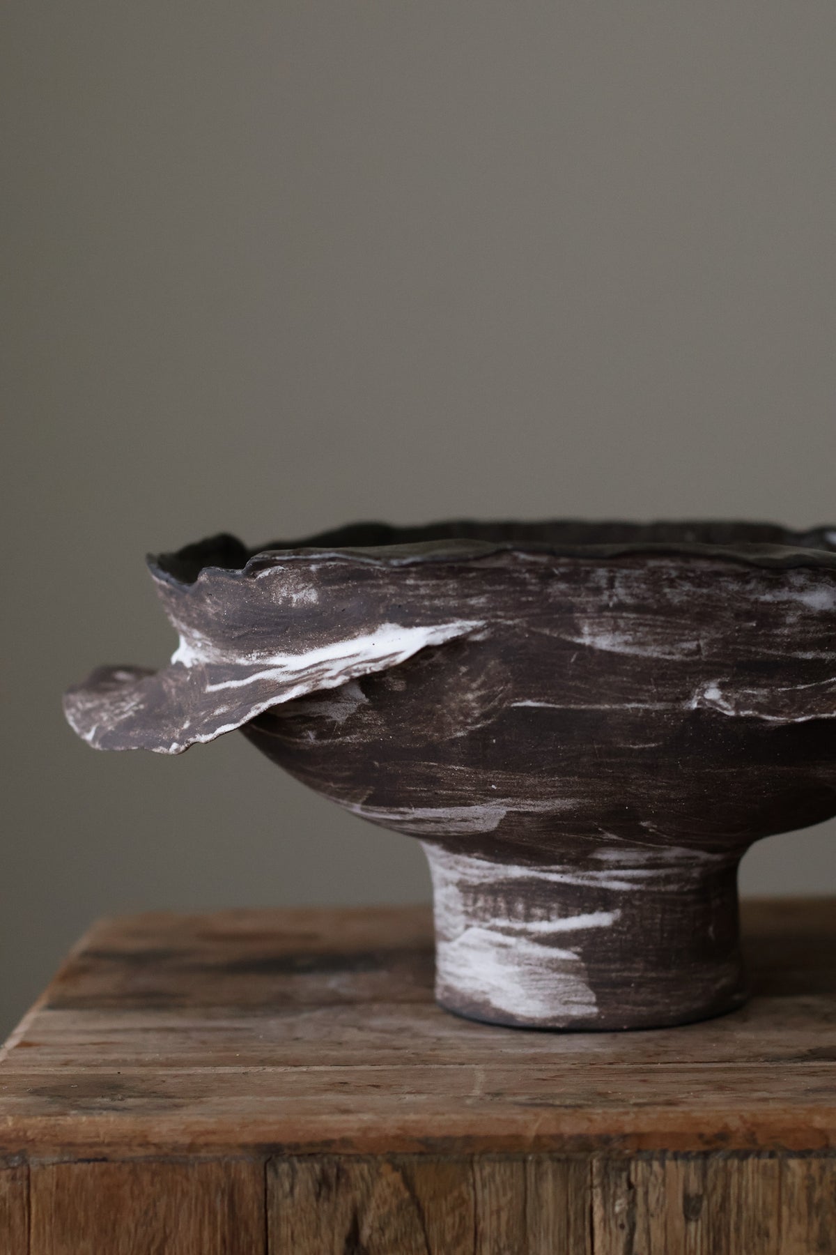 Layered Brown Pedestal Bowl is a Handcrafted ceramic piece with raw, textured dark clay finish and organic wavy rim, featuring sculptural asymmetry