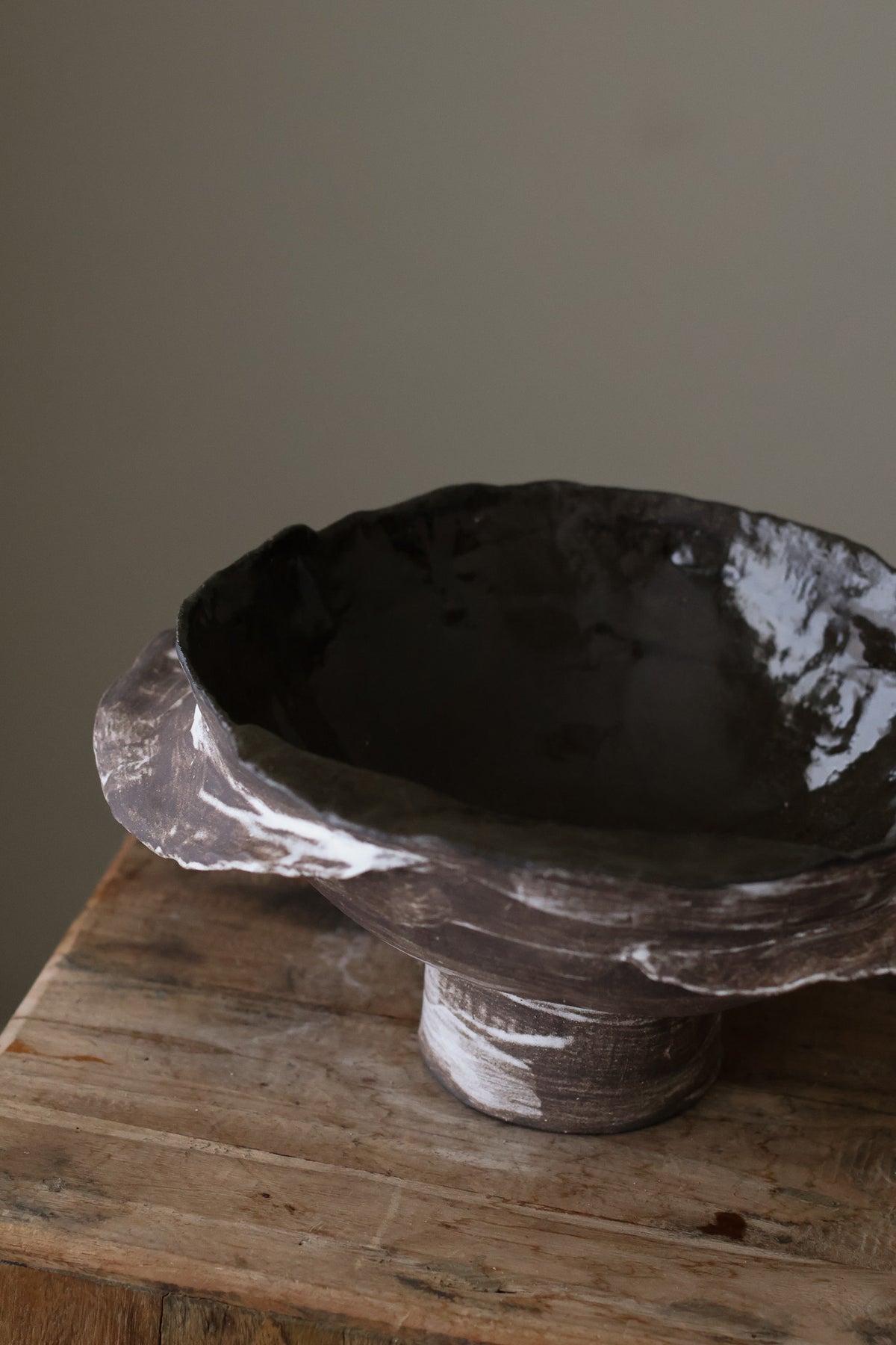 Layered Brown Pedestal Bowl is a Handcrafted ceramic piece with raw, textured dark clay finish and organic wavy rim, featuring sculptural asymmetry