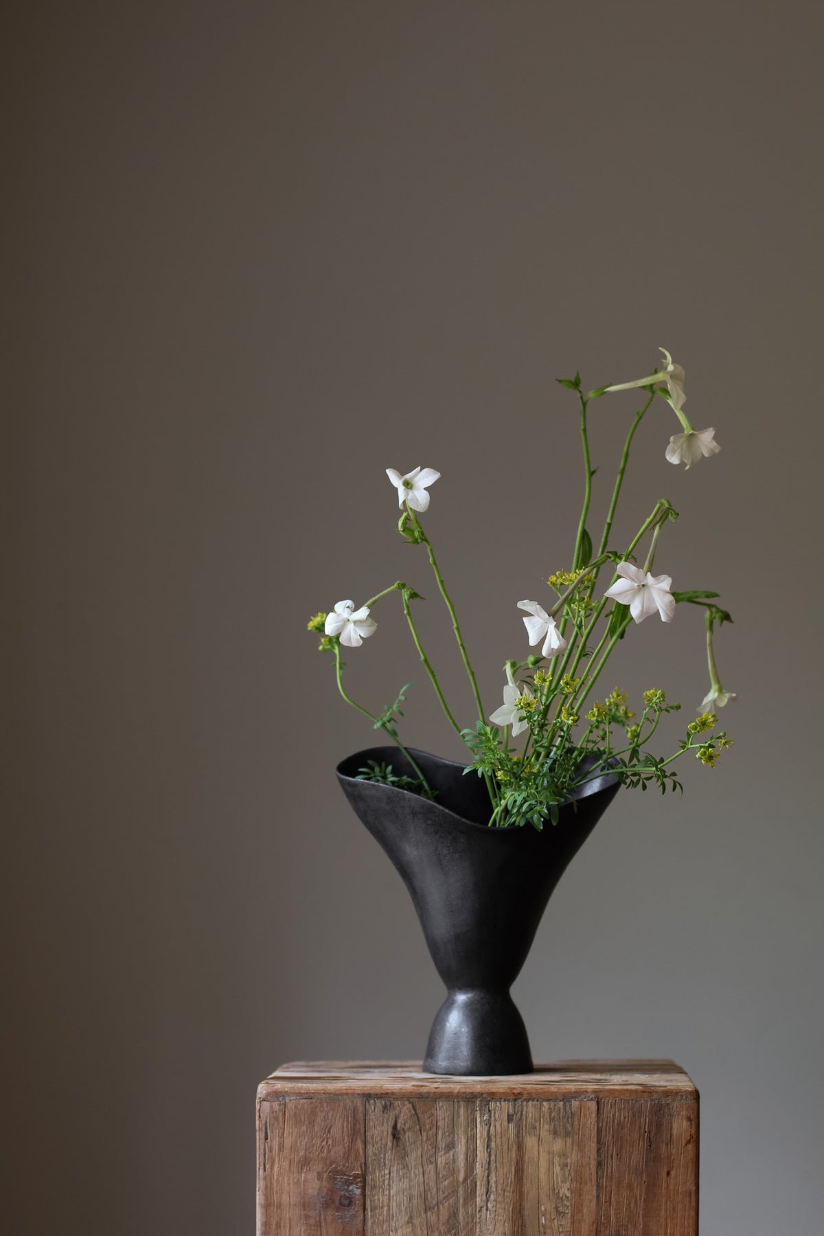 The Aires Sculptural Vessel INK by Karen Quirion, featuring fluid curves and a textured black exterior, creating a romantic yet modern aesthetic. Perfect for floral arrangements and as a striking interior centerpiece.
