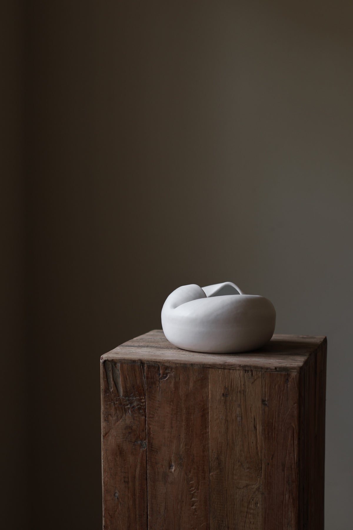 Sculptural white porcelain vase with fluid form and distinctive fold dividing it into asymmetrical halves, modern centerpiece.