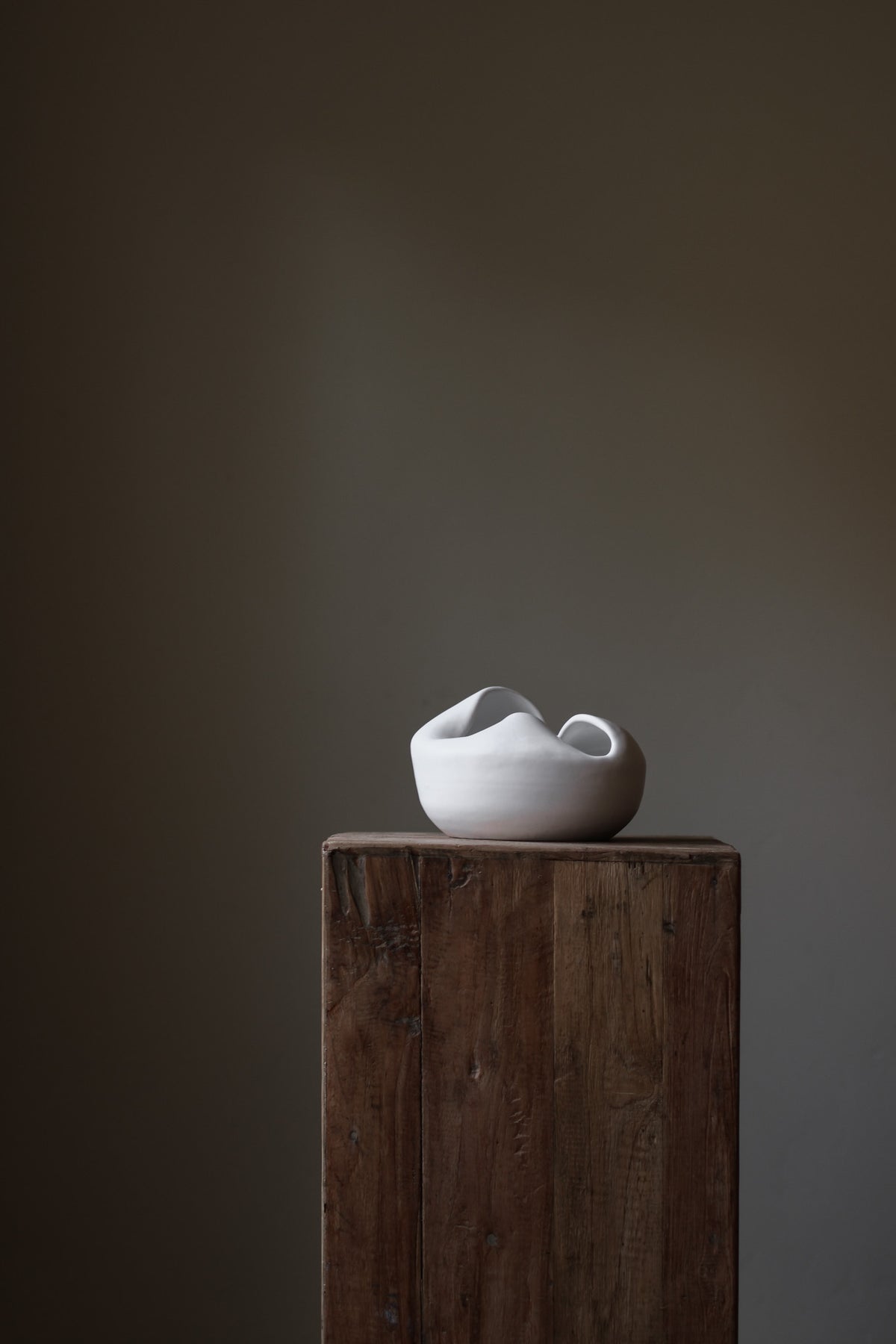 Sculptural white porcelain vase with fluid form and distinctive fold dividing it into asymmetrical halves, modern centerpiece.