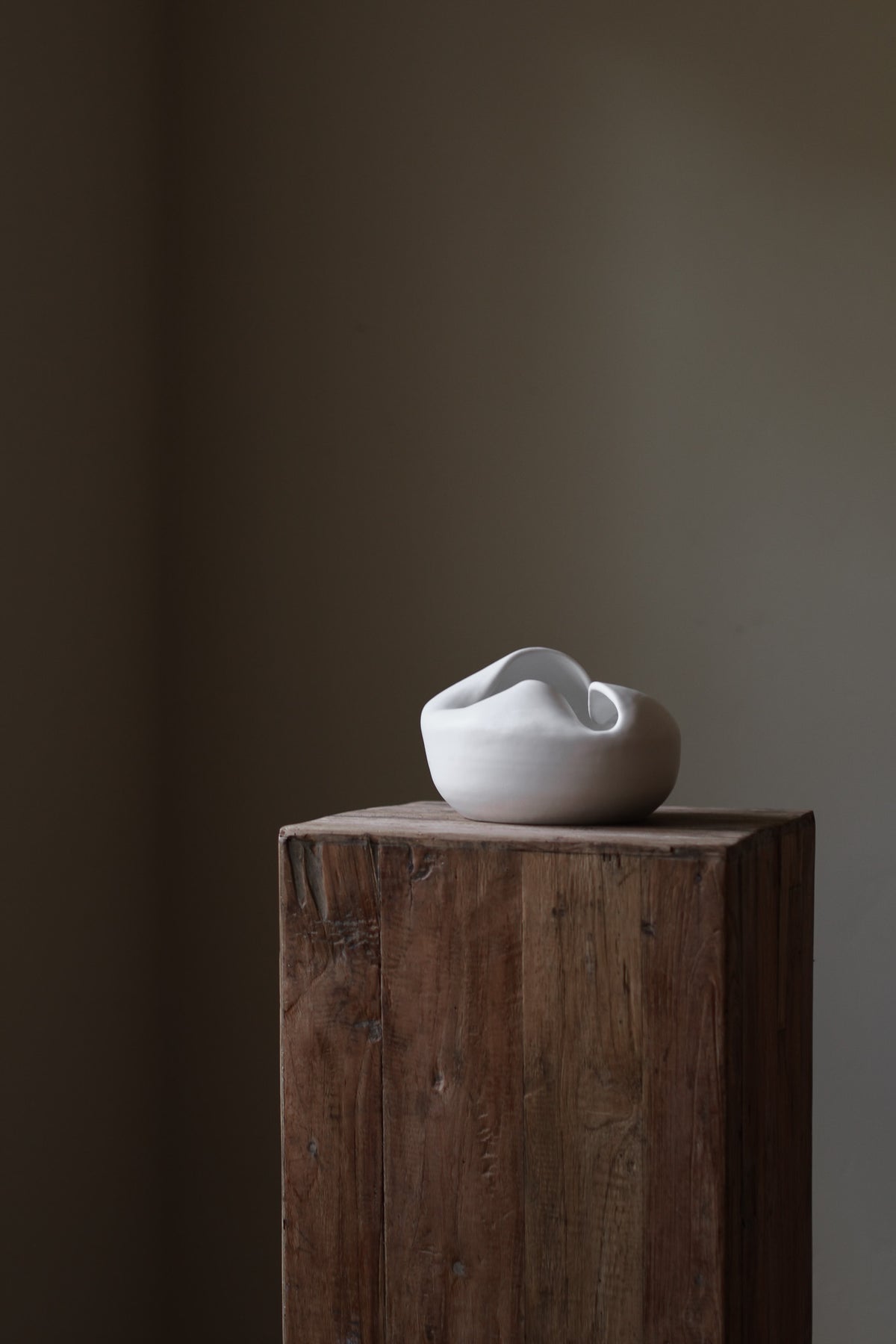 Sculptural white porcelain vase with fluid form and distinctive fold dividing it into asymmetrical halves, modern centerpiece.