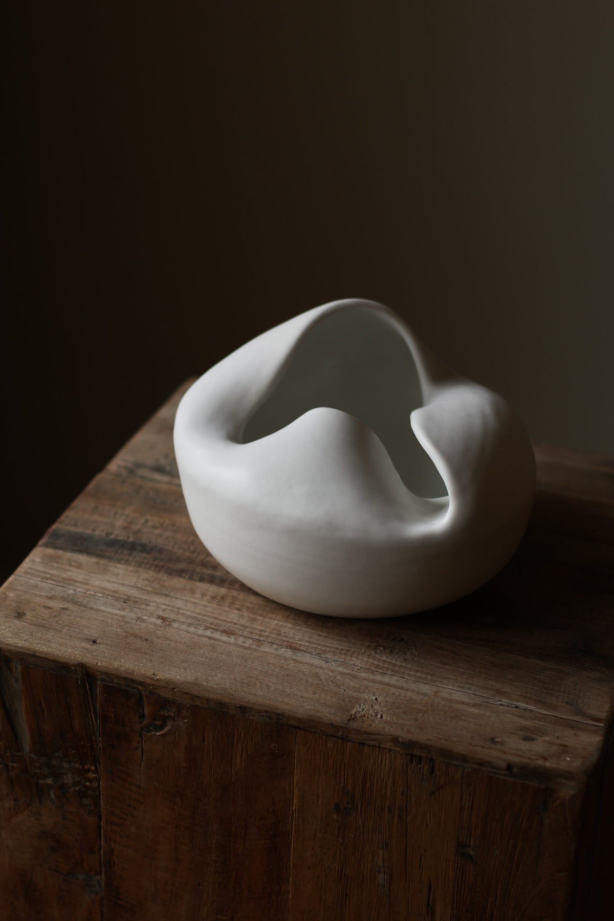 Sculptural white porcelain vase with fluid form and distinctive fold dividing it into asymmetrical halves, modern centerpiece.