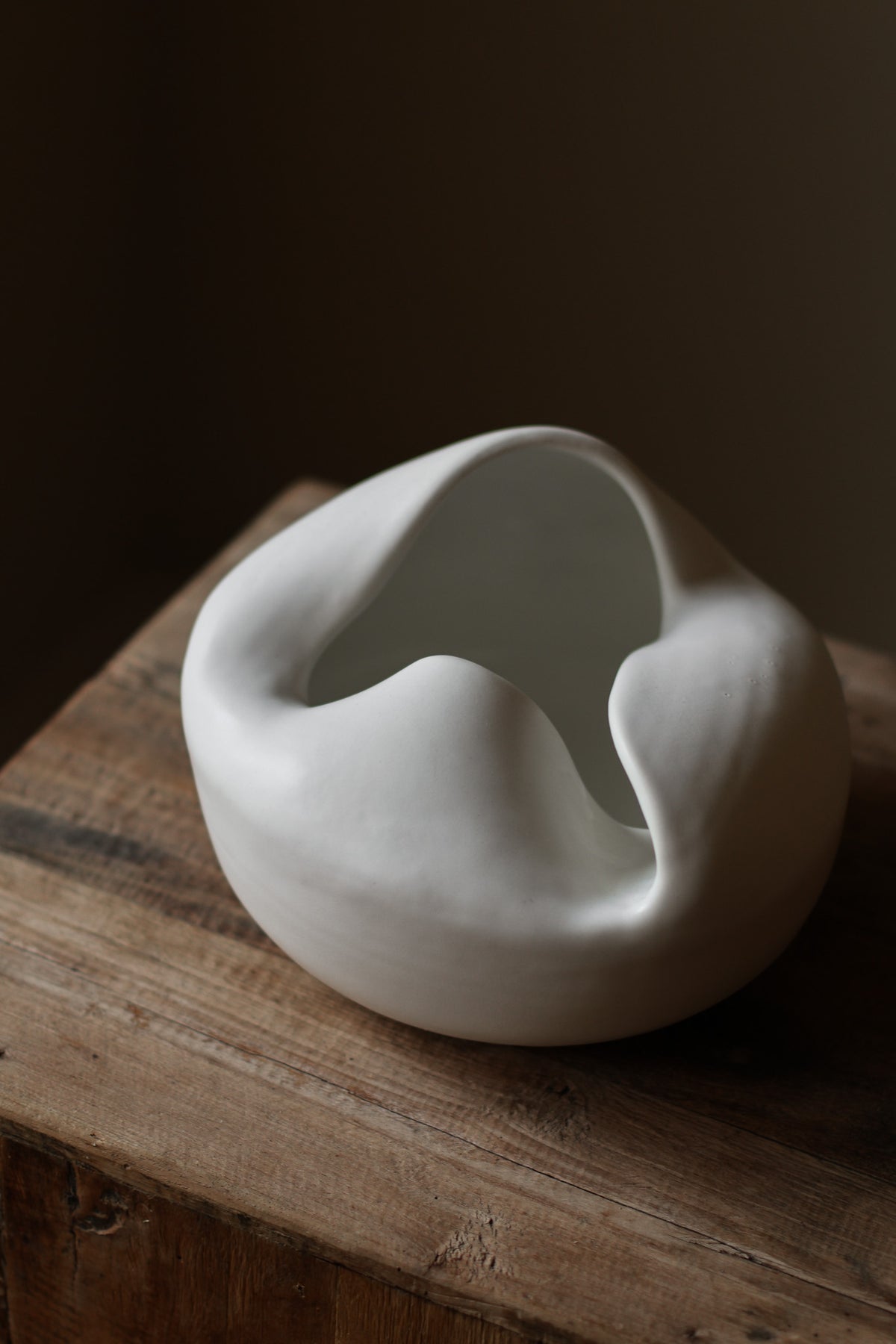 Sculptural white porcelain vase with fluid form and distinctive fold dividing it into asymmetrical halves, modern centerpiece.