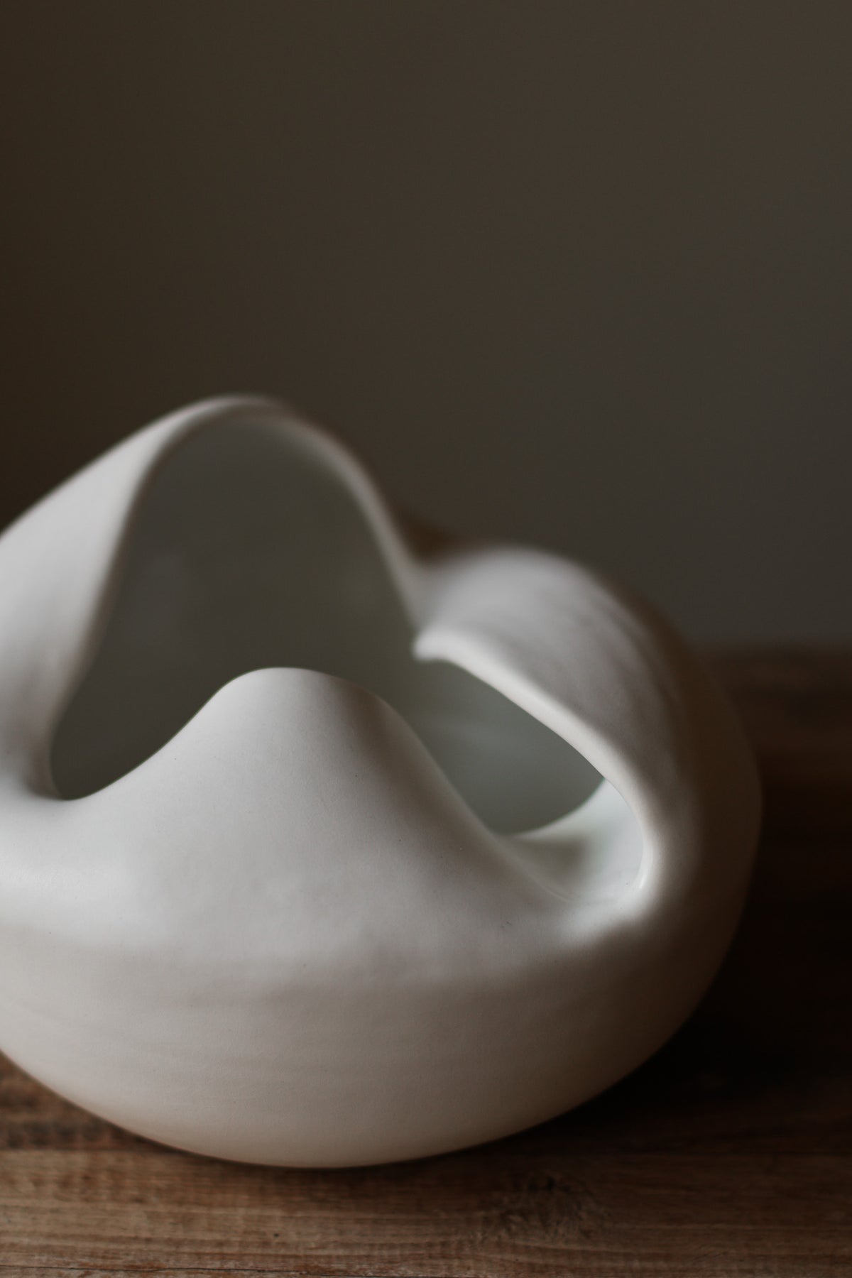 Sculptural white porcelain vase with fluid form and distinctive fold dividing it into asymmetrical halves, modern centerpiece.