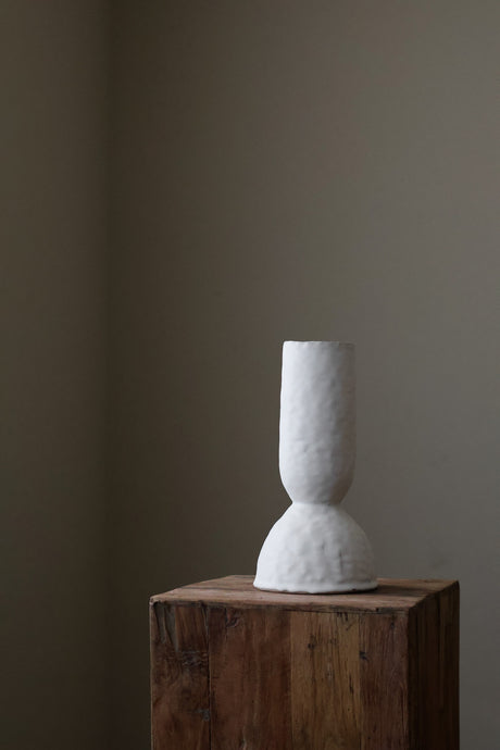 Modern sculptural vase in bright white, featuring a distinctive, textured surface and a simple, cylindrical form with a slightly flared base.