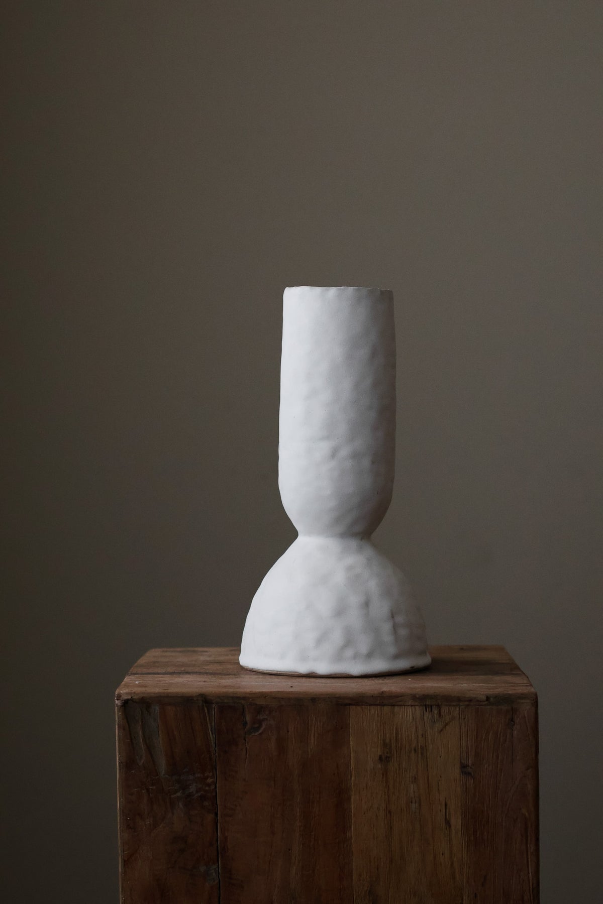 Modern sculptural vase in bright white, featuring a distinctive, textured surface and a simple, cylindrical form with a slightly flared base.