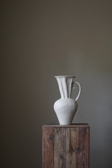 Hand-built, tall, off-white vase with a heavily textured, ribbed surface, a slightly flared rim, and a curved handle. 