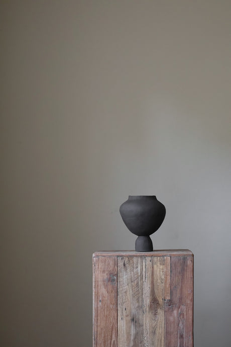 A hand-built, matte white sculptural vase by Hana. The vase features a generously rounded, almost bulbous body that tapers dramatically to a slender, short neck. The surface of the vase exhibits a subtle, textured quality, suggesting the artist's hand-building process.  