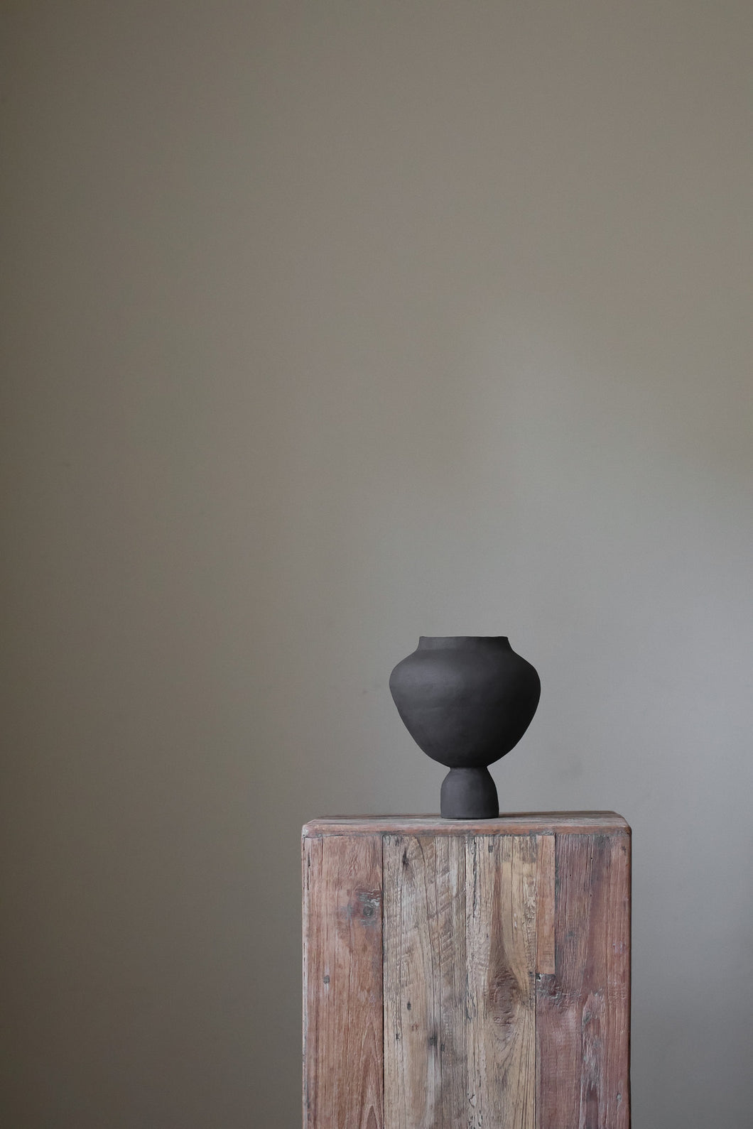 A hand-built, matte white sculptural vase by Hana. The vase features a generously rounded, almost bulbous body that tapers dramatically to a slender, short neck. The surface of the vase exhibits a subtle, textured quality, suggesting the artist's hand-building process.  