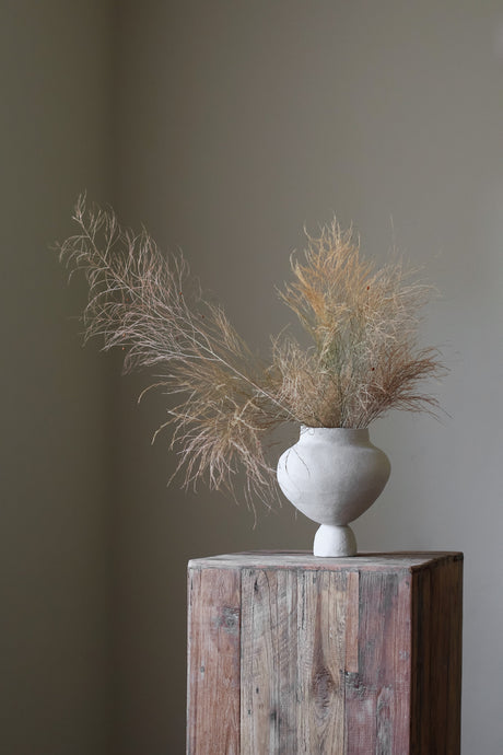 A hand-built, matte white sculptural vase by Hana. The vase features a generously rounded, almost bulbous body that tapers dramatically to a slender, short neck. The surface of the vase exhibits a subtle, textured quality, suggesting the artist's hand-building process.  