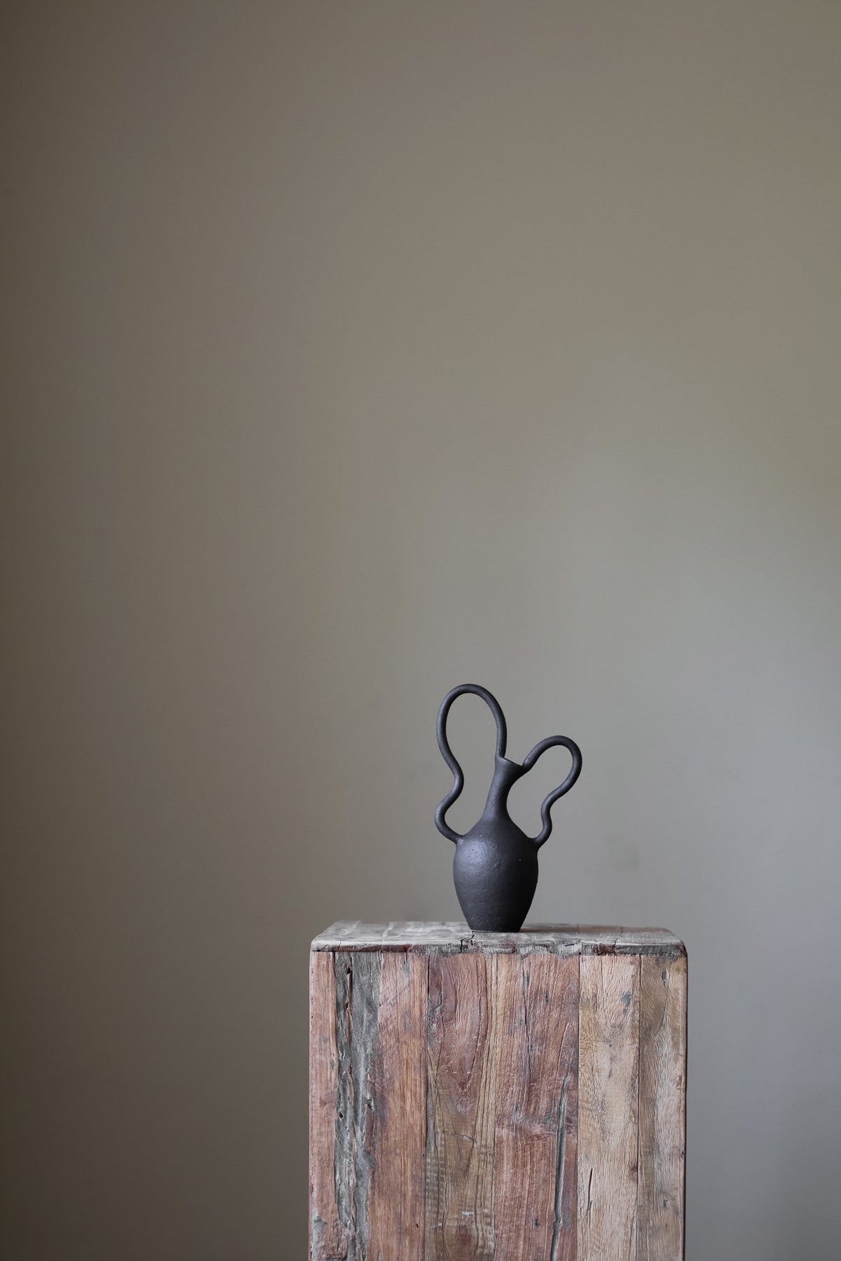 Hand-built dark ceramic vase with a textured, matte finish and two dramatically looped, sculptural handles. 