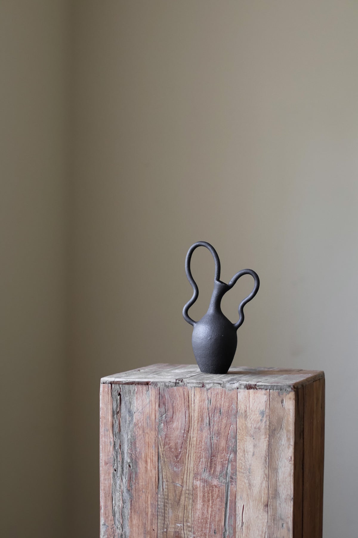 Hand-built dark ceramic vase with a textured, matte finish and two dramatically looped, sculptural handles. 