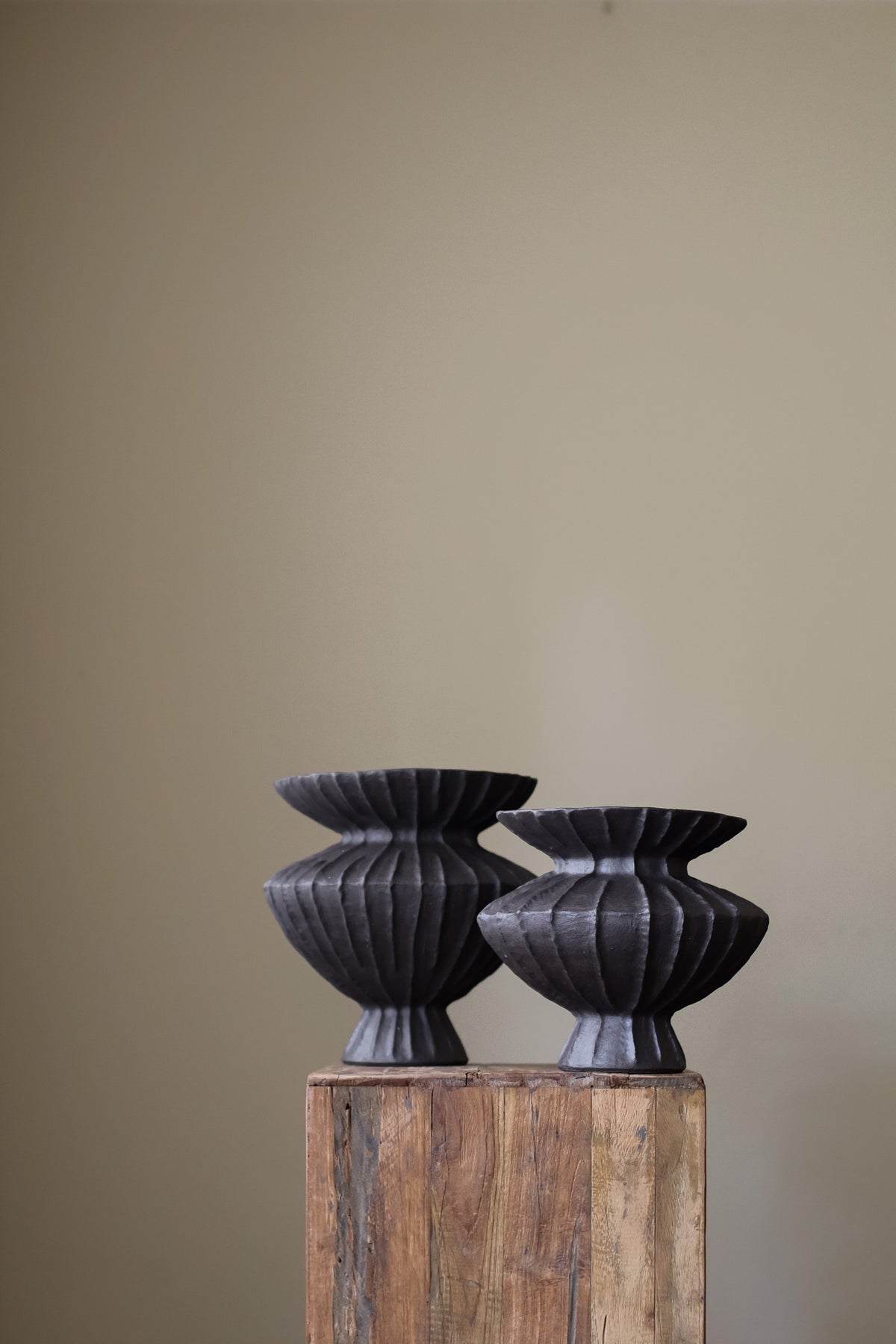 Hand-built dark ceramic vase with a heavily textured, ribbed surface and a slightly flared rim, holding two slender.