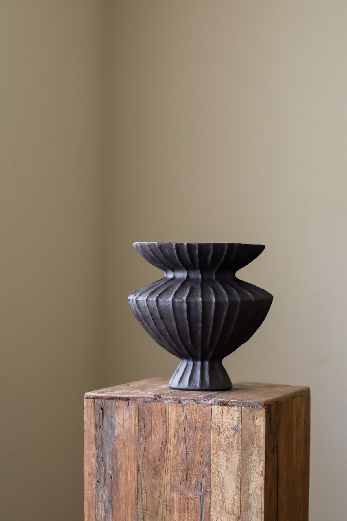 Hand-built dark ceramic vase with a heavily textured, ribbed surface and a slightly flared rim, holding two slender.