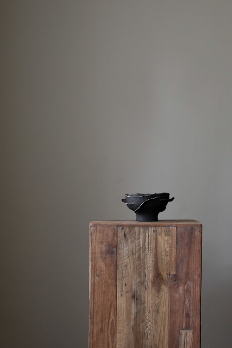 Contemporary sculptural bowl in a deep, dark tone, featuring an organic, irregular rim with silver accents and a rough, textured finish