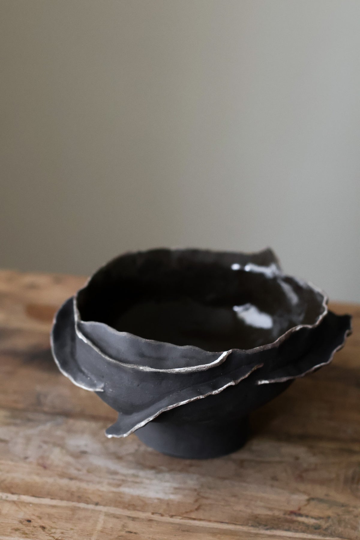 Contemporary sculptural bowl in a deep, dark tone, featuring an organic, irregular rim with silver accents and a rough, textured finish