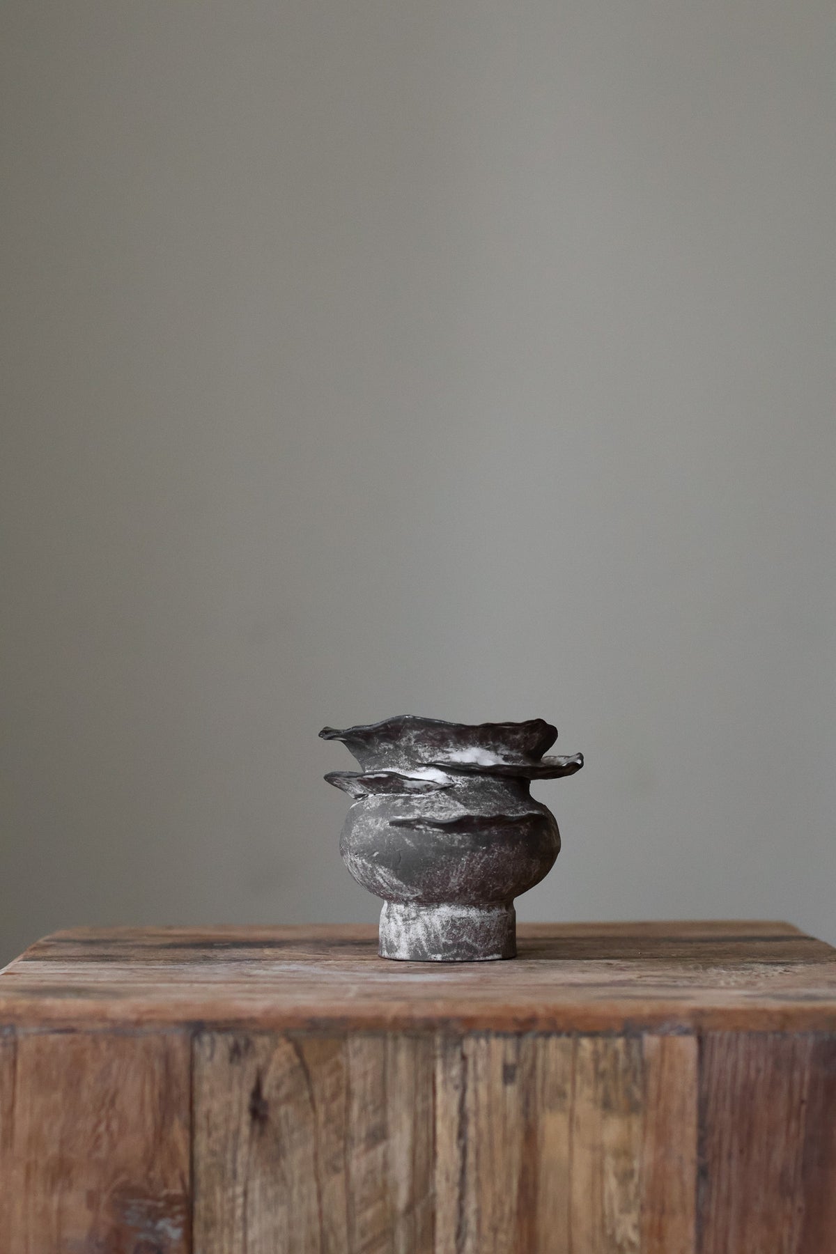 Contemporary sculptural vase in a dark, weathered tone, featuring a unique, layered, and ruffled top design with a rough, organic aesthetic.
