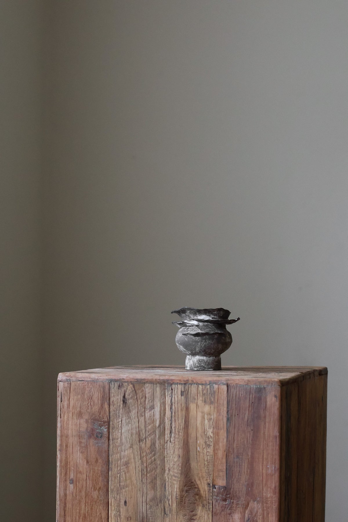 Contemporary sculptural vase in a dark, weathered tone, featuring a unique, layered, and ruffled top design with a rough, organic aesthetic.