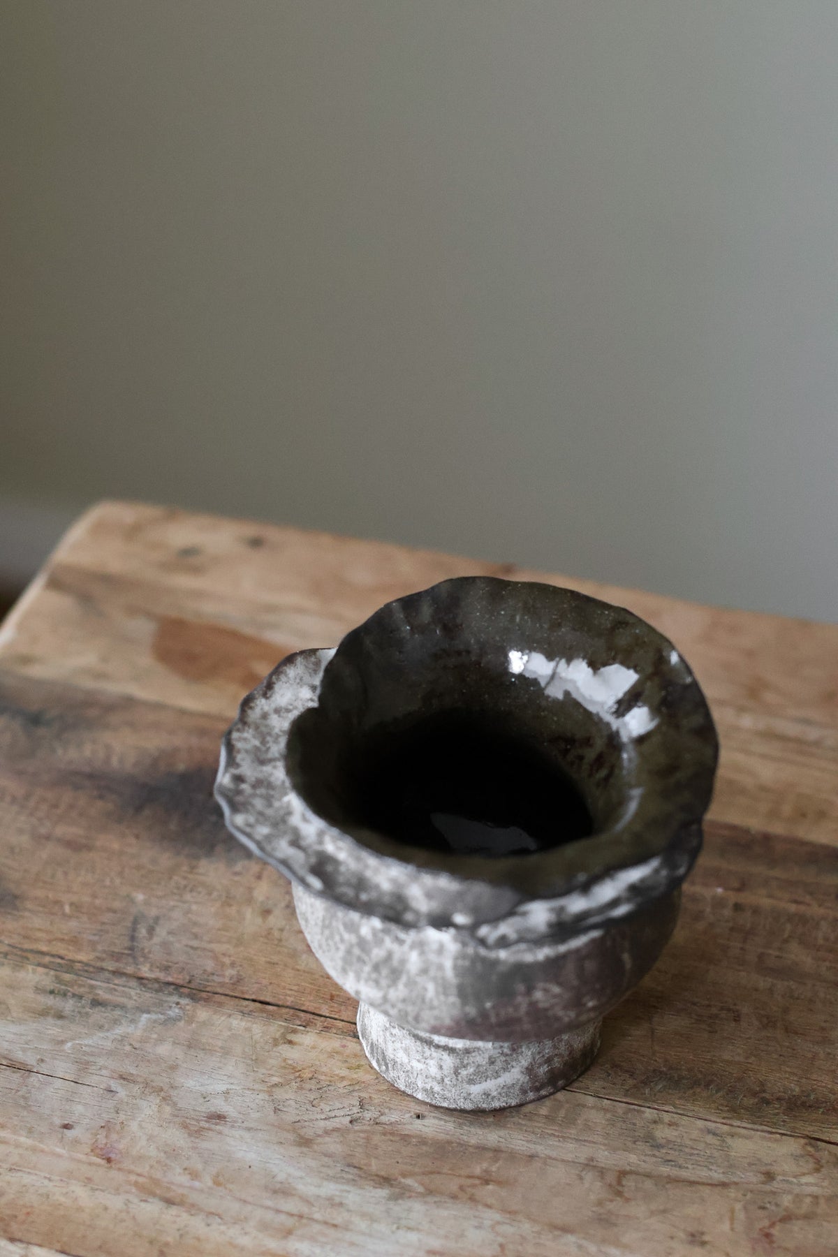 Contemporary sculptural vase in a dark, weathered tone, featuring a unique, layered, and ruffled top design with a rough, organic aesthetic.