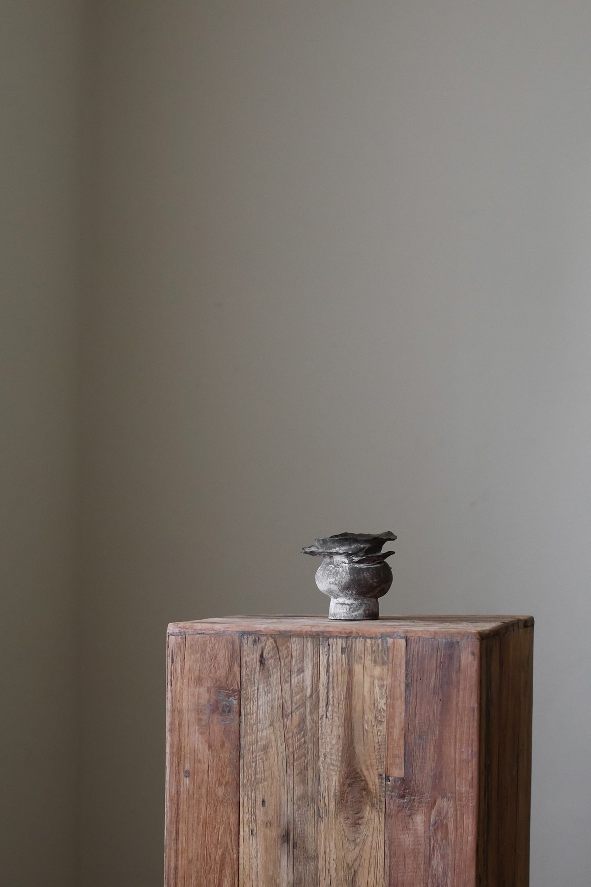 Contemporary sculptural vase in a dark, weathered tone, featuring a unique, layered, and ruffled top design with a rough, organic aesthetic.