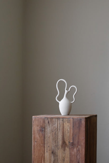 Contemporary sculptural vase in bright white, featuring two unique, flowing handles and a simple, rounded body.