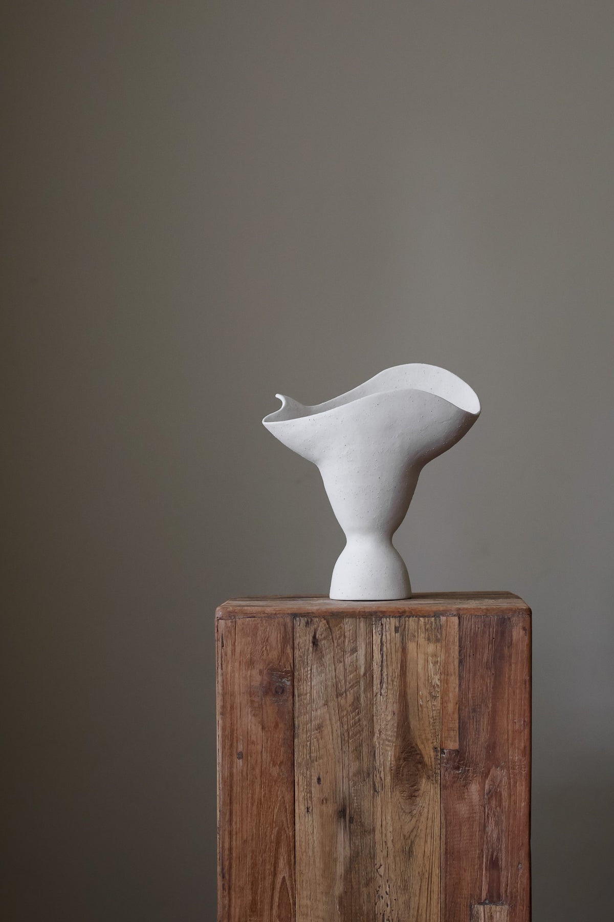 This hand-built ceramic piece exhibits a captivating organic form, reminiscent of a flower blossom gracefully opening. The vase's body begins with a slender base, gradually expanding outward and culminating in a dramatically flared, undulating rim. The rim itself is a work of art, with a gently ruffled edge that evokes the delicate petals of a flower. 