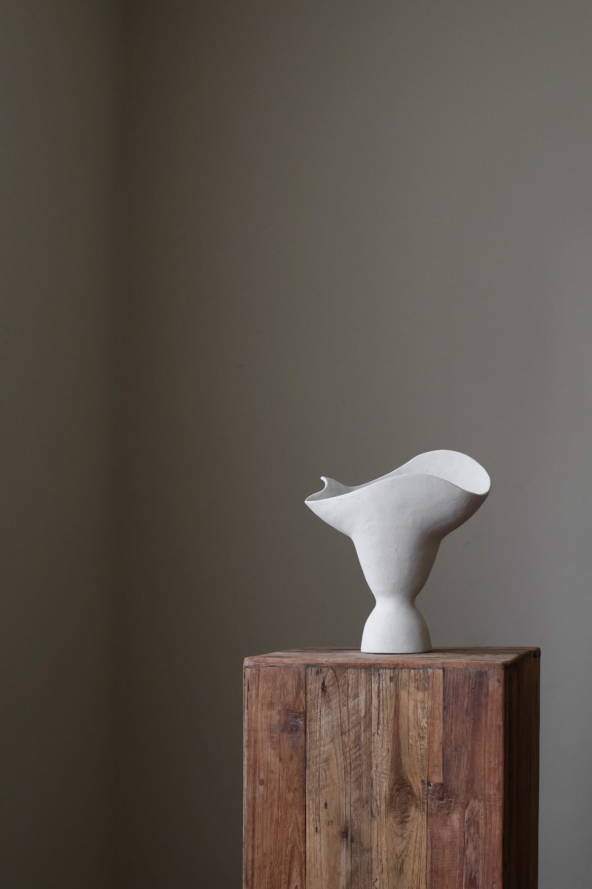 This hand-built ceramic piece exhibits a captivating organic form, reminiscent of a flower blossom gracefully opening. The vase's body begins with a slender base, gradually expanding outward and culminating in a dramatically flared, undulating rim. The rim itself is a work of art, with a gently ruffled edge that evokes the delicate petals of a flower. 