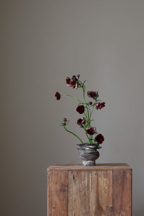 Contemporary sculptural vase in a dark, weathered tone, featuring a unique, layered, and ruffled top design with a rough, organic aesthetic.