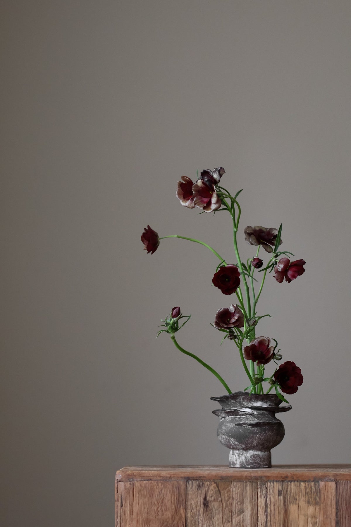 Contemporary sculptural vase in a dark, weathered tone, featuring a unique, layered, and ruffled top design with a rough, organic aesthetic.