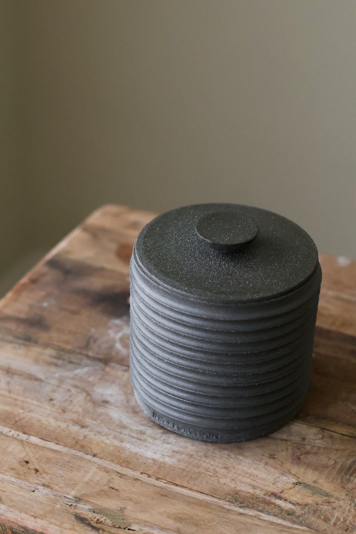 Textured cylindrical container with a removable lid, featuring a matte finish and a modern, minimalist design.