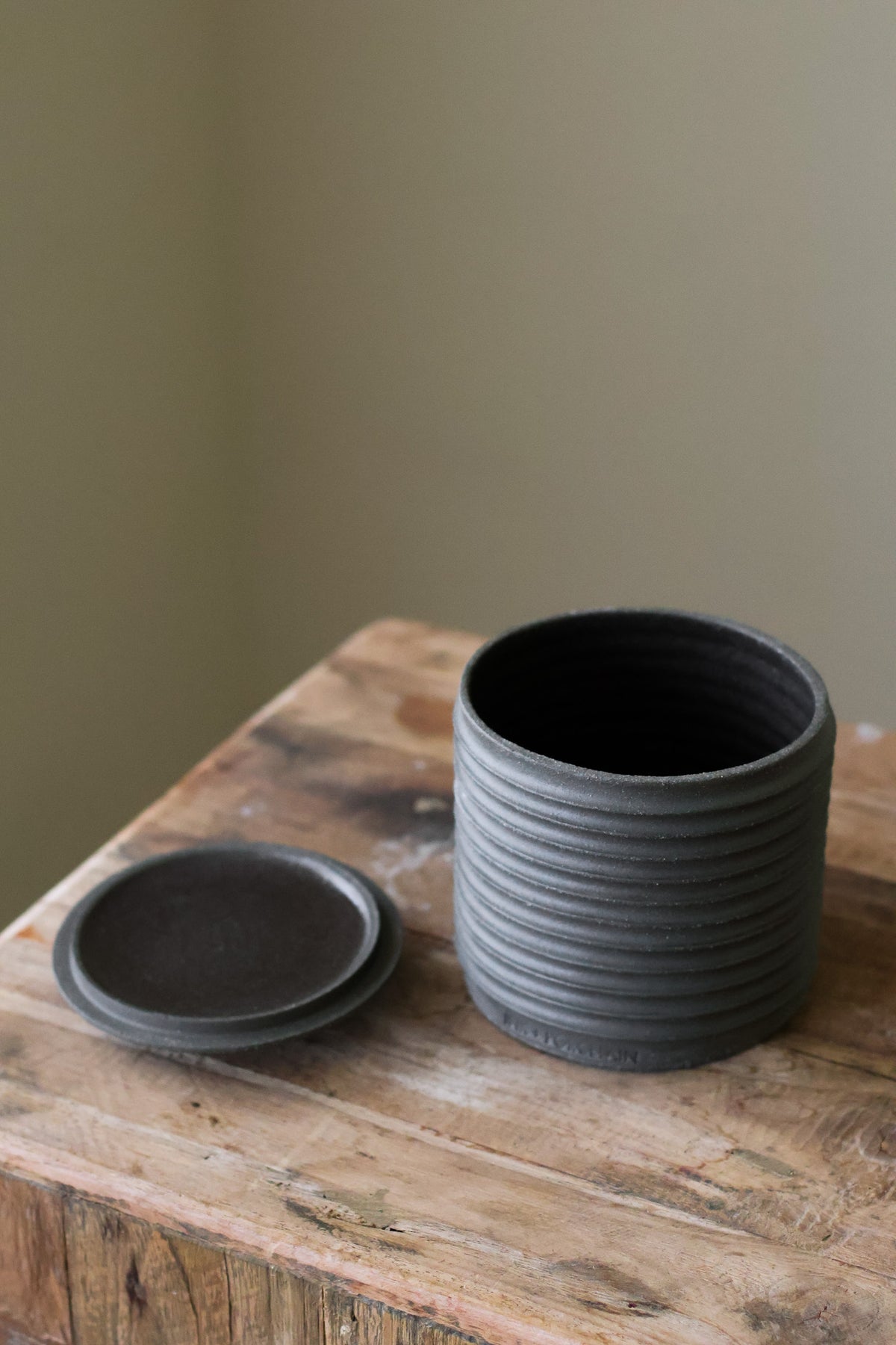 Textured cylindrical container with a removable lid, featuring a matte finish and a modern, minimalist design.