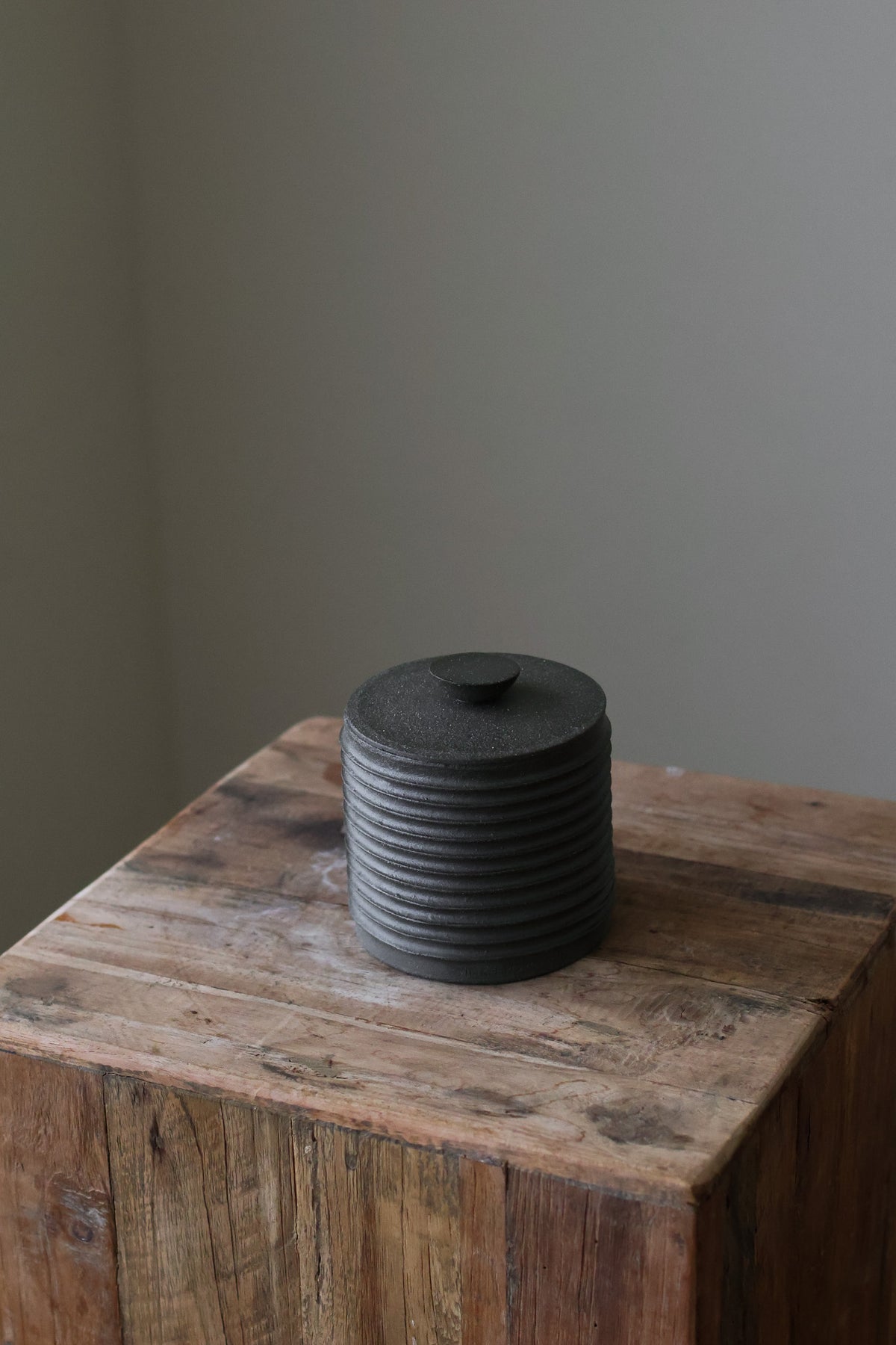 Textured cylindrical container with a removable lid, featuring a matte finish and a modern, minimalist design.