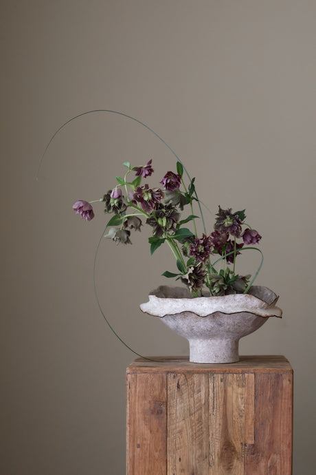 The bowl showcases delicate and intricate ruffled layers of light gray and white ceramic, creating a sense of graceful movement. The texture of the ceramic is subtle and tactile. Handcrafted by Bay Area artist Virginia May, this piece reflects the artful collection that captures layers of subtle texture.