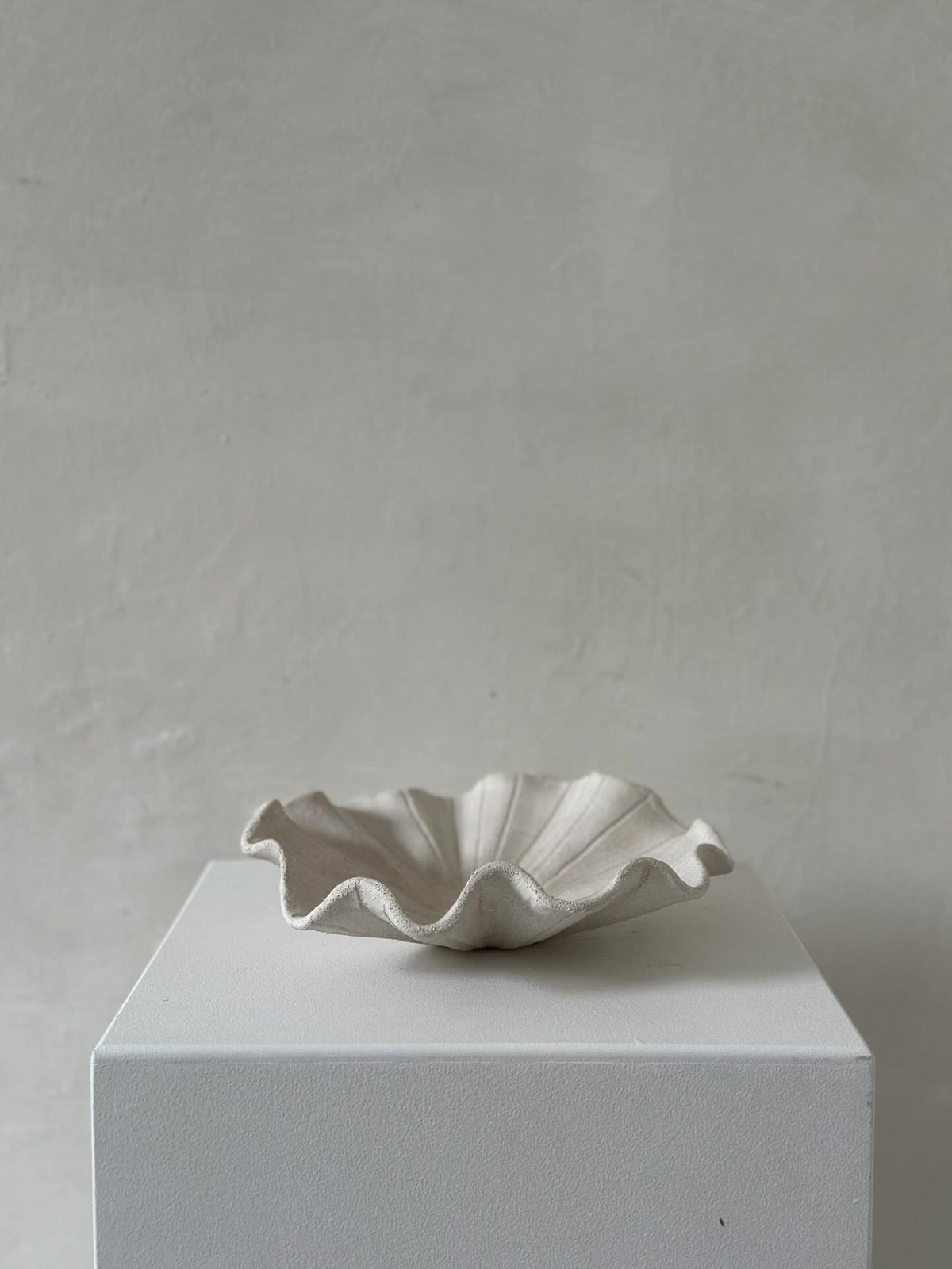 A low handmade ceramic tray with a wavy edge. The tray has a light brown, slightly textured surface 