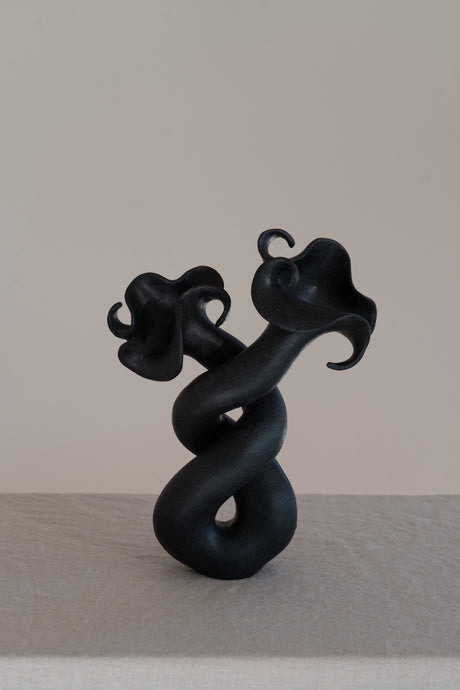 This matte black, textured ceramic vessel features curvaceous forms and a soft brutalist style, embodying nature's enchanting beauty and striking contrast in home decor.
