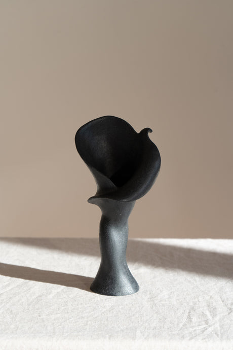  A matte black ceramic vase inspired by the Calla Lily, blending floral curves with bold stoneware. Features a glazed interior, perfect as a striking modern decor piece.